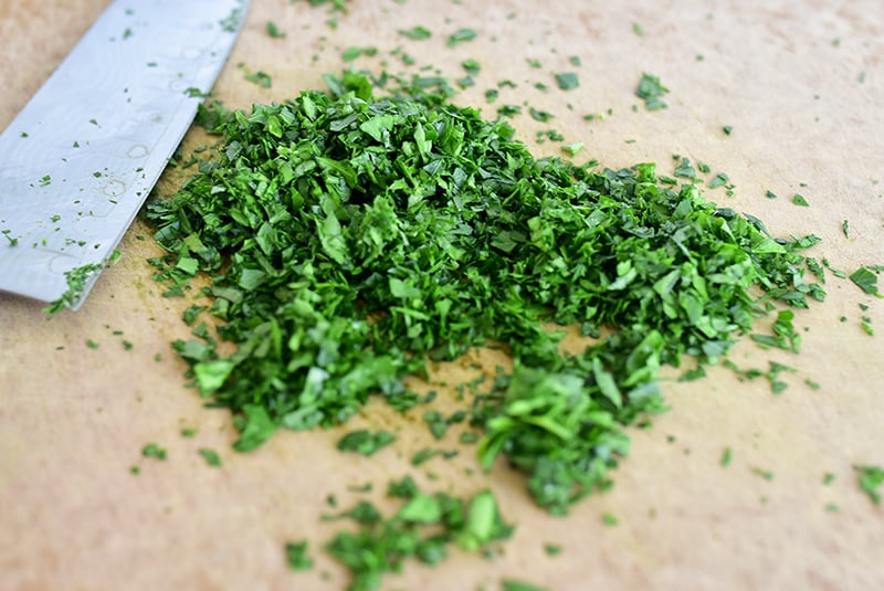 Finely chopped green parsley on a chopping board with a silver knife