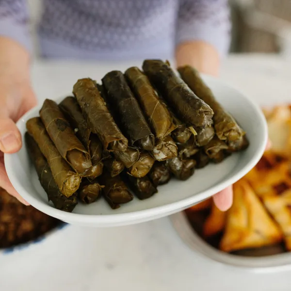 Lebanese stuffed grape leaves on a white platter served by Maureen Abood's hands