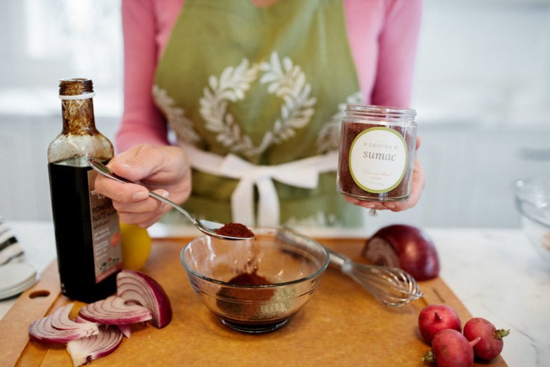 Fattoush salad dressing ingredients with a jar of sumac and a spoon in Maureen Abood's hand