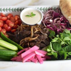Beef shawarma on a platter with vegetables and tahini sauce