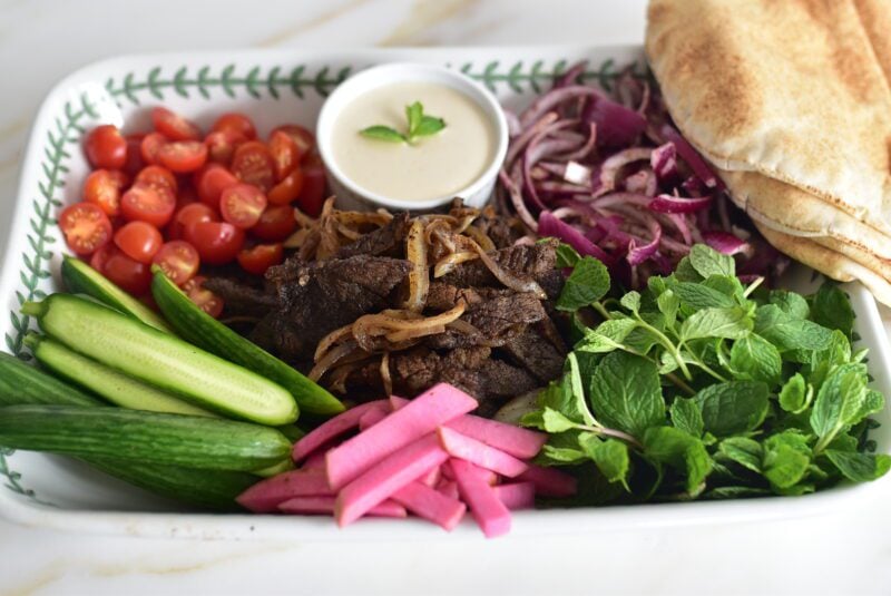 Beef shawarma on a platter with vegetables and tahini sauce