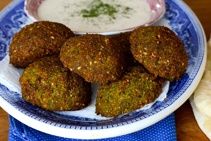 Falafel fritters on a blue platter with a small bowl of tahini sauce