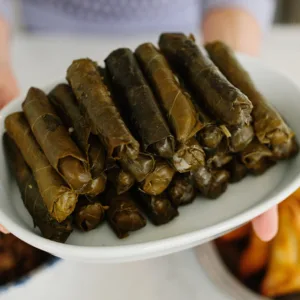 Lebanese stuffed grapeleaf rolls on a white platter with hands holding it