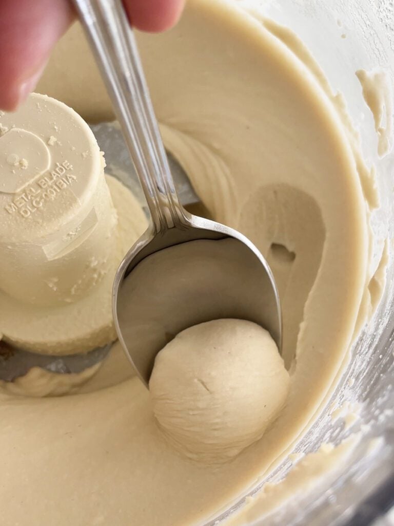 Hummus being scooped from a food processor with a spoon.