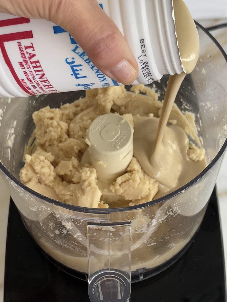 Tahini being poured into the food processor to make hummus.