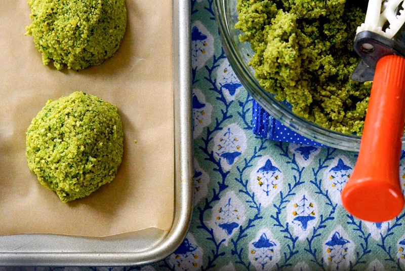 Falafel formed in a ball on a sheet pan with an orange scoop
