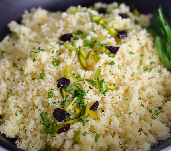 Couscous in a black dish with dried cherried and pistachios on top