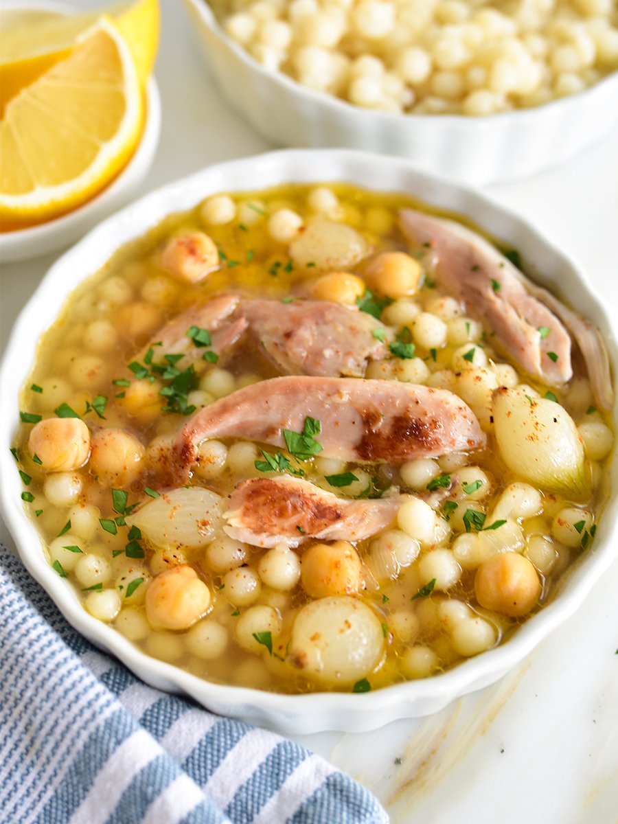 Lebanese moghrabieh in a white dish with chicken, onions, chickpeas