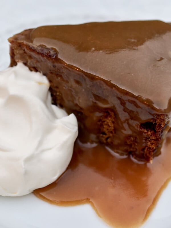 A wedge of brown sticky date cake covered with glossy caramel sauce and a dollop of whipped cream