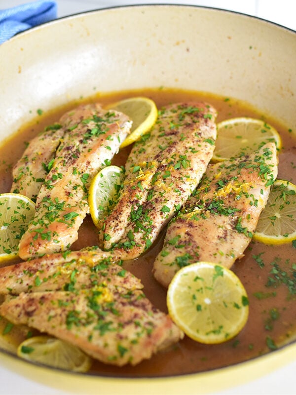 Chicken with lemons and sauce in a skillet with a blue towel