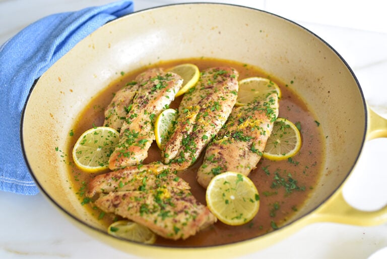 Chicken with lemons and sauce in a skillet with a blue towel