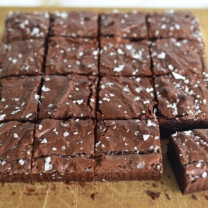 Olive oil brownies on a sheet of parchment cut in squares, with sea salt on top