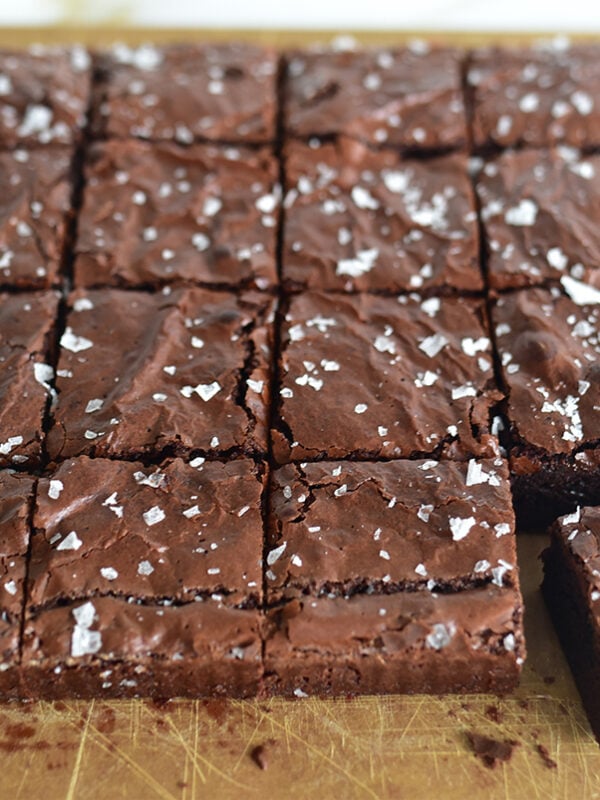 Olive oil brownies on a sheet of parchment cut in squares, with sea salt on top