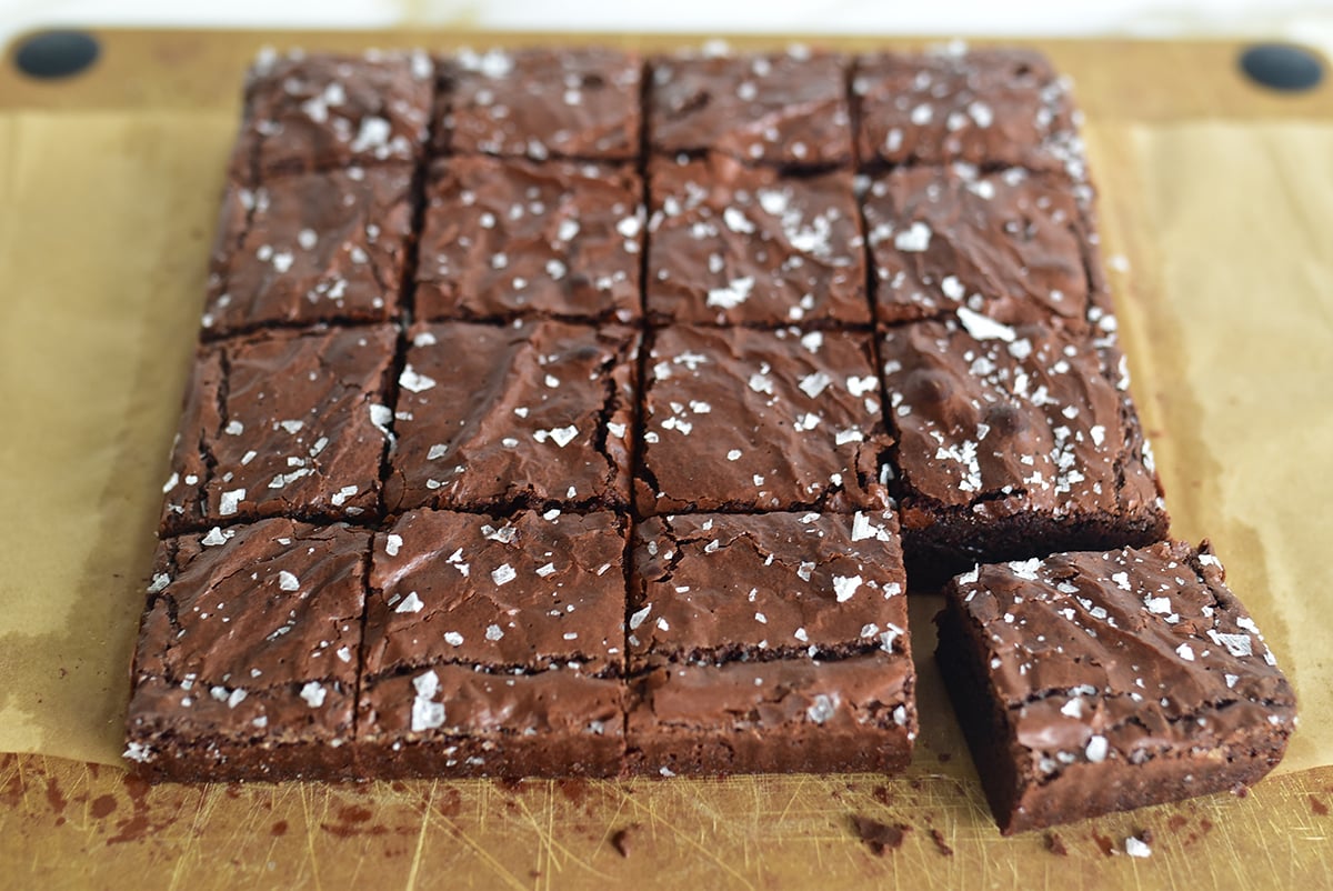 Olive oil brownies on a sheet of parchment cut in squares, with sea salt on top