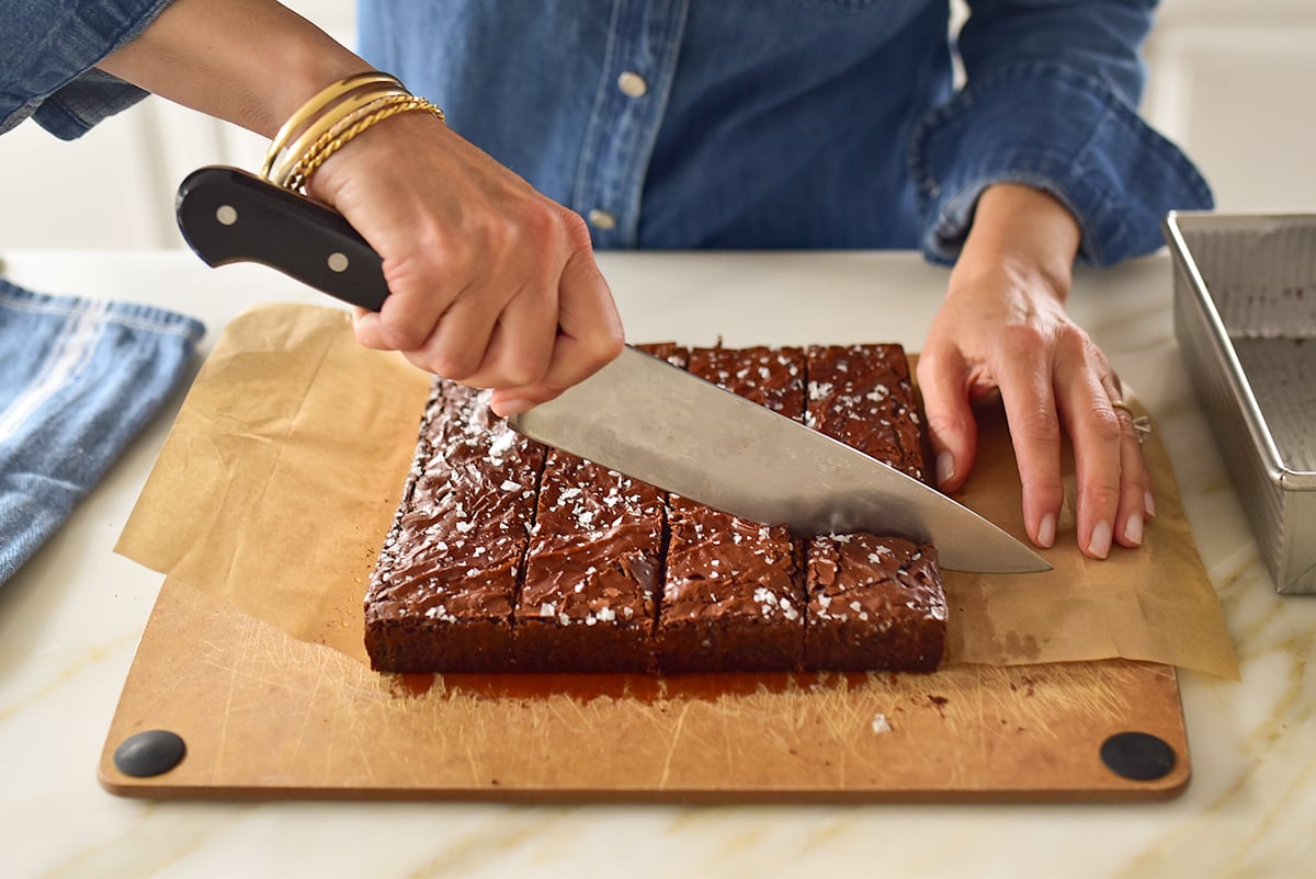 A hand using a chef's knife to cut brownies on a cutting board