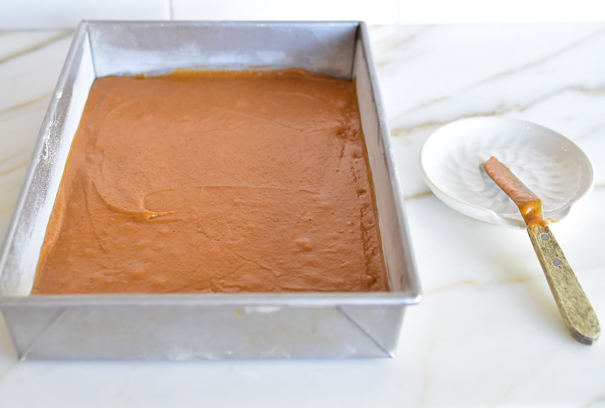 Pumpkin bar batter in a metal pan with offset spatula on the side on a marble counter