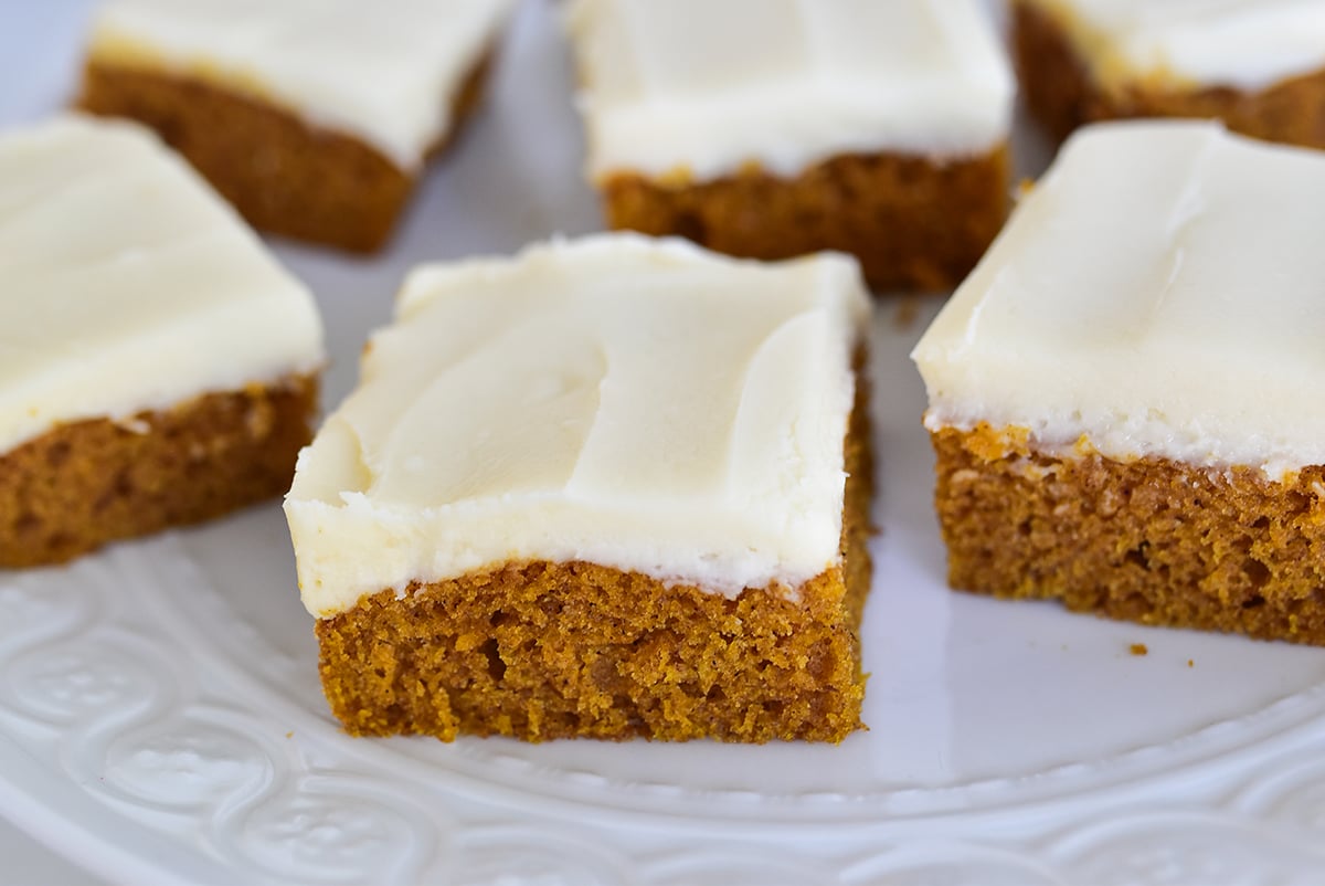 Pumpkin bars with white cream cheese frosting slices on a white plate
