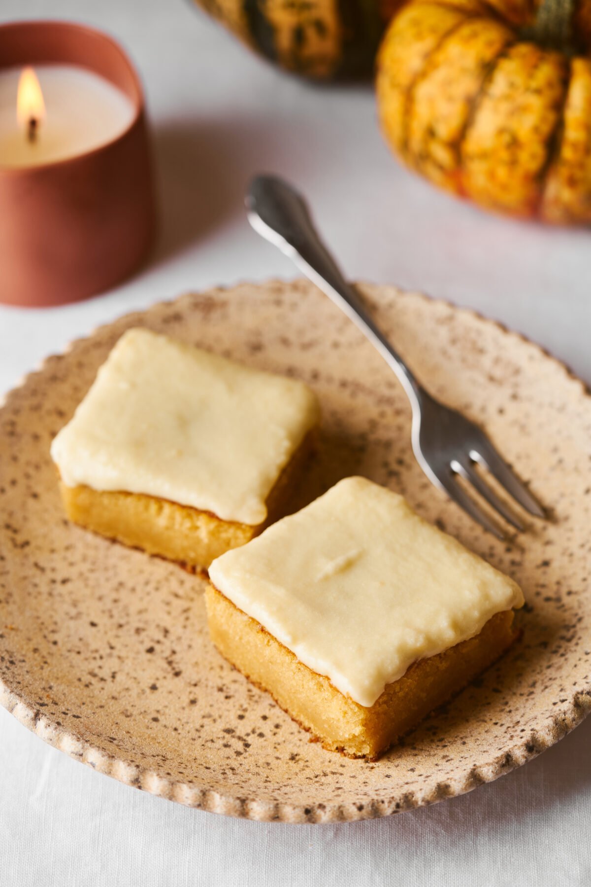 Frosted pumpkin bars on a tan plate with a fork and candle in the background