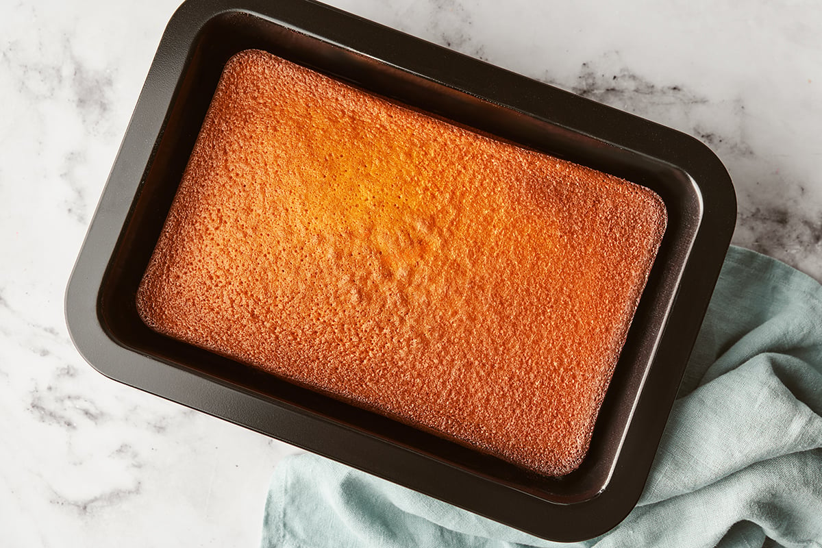 Baked pumpkin cake in a dark cake pan with a light blue towel on the side