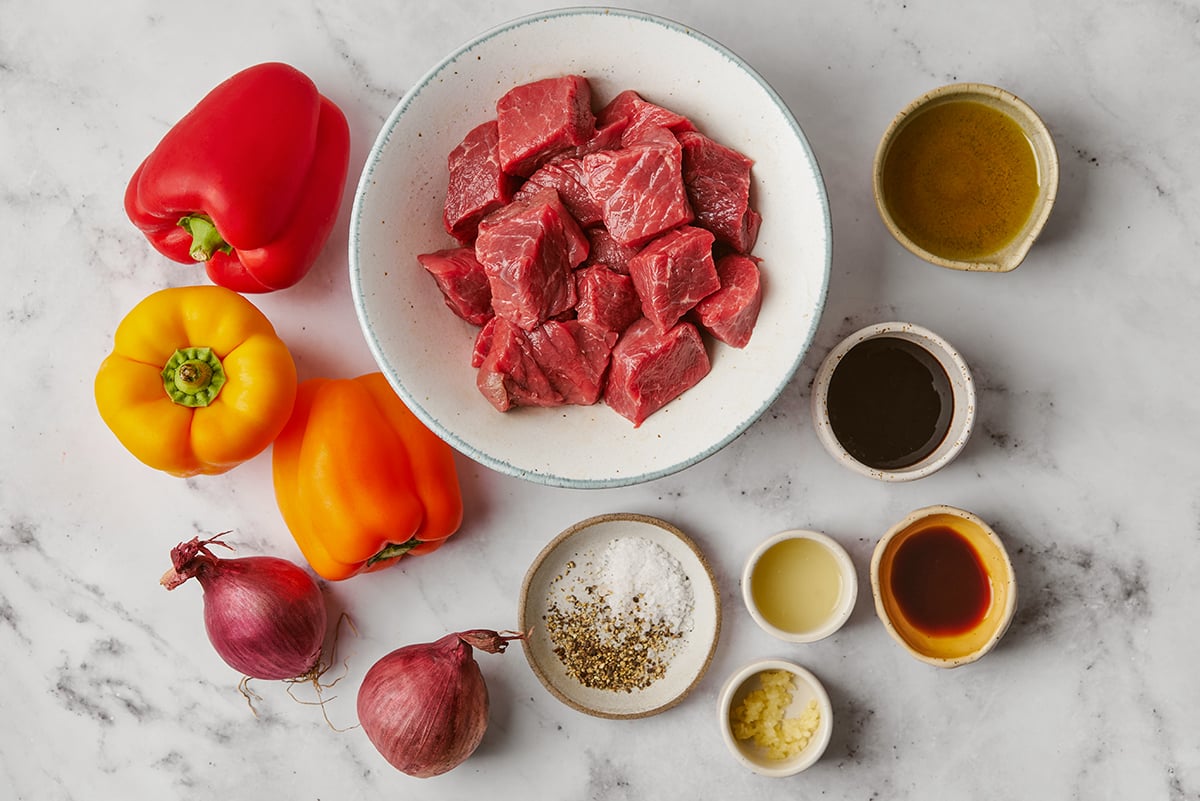 Beef shish kebab ingredients in bowls on a marble surface