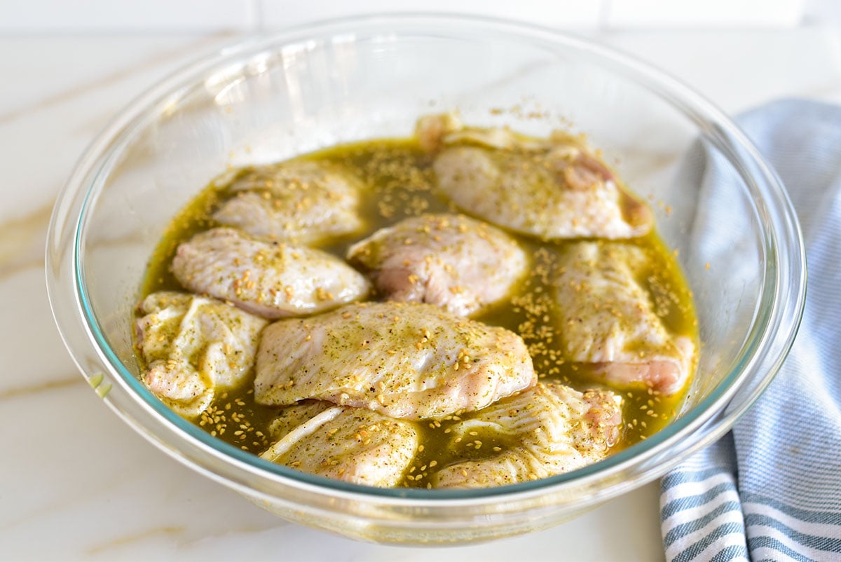 Chicken pieces in marinade in a glass bowl with blue towel alongside