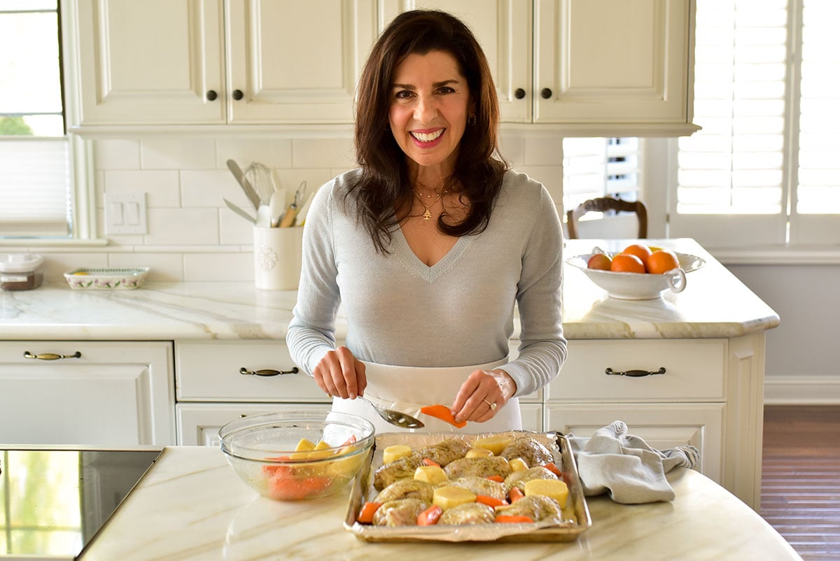 Maureen Abood placing chicken and vegetables on a sheet pan in the kitchen