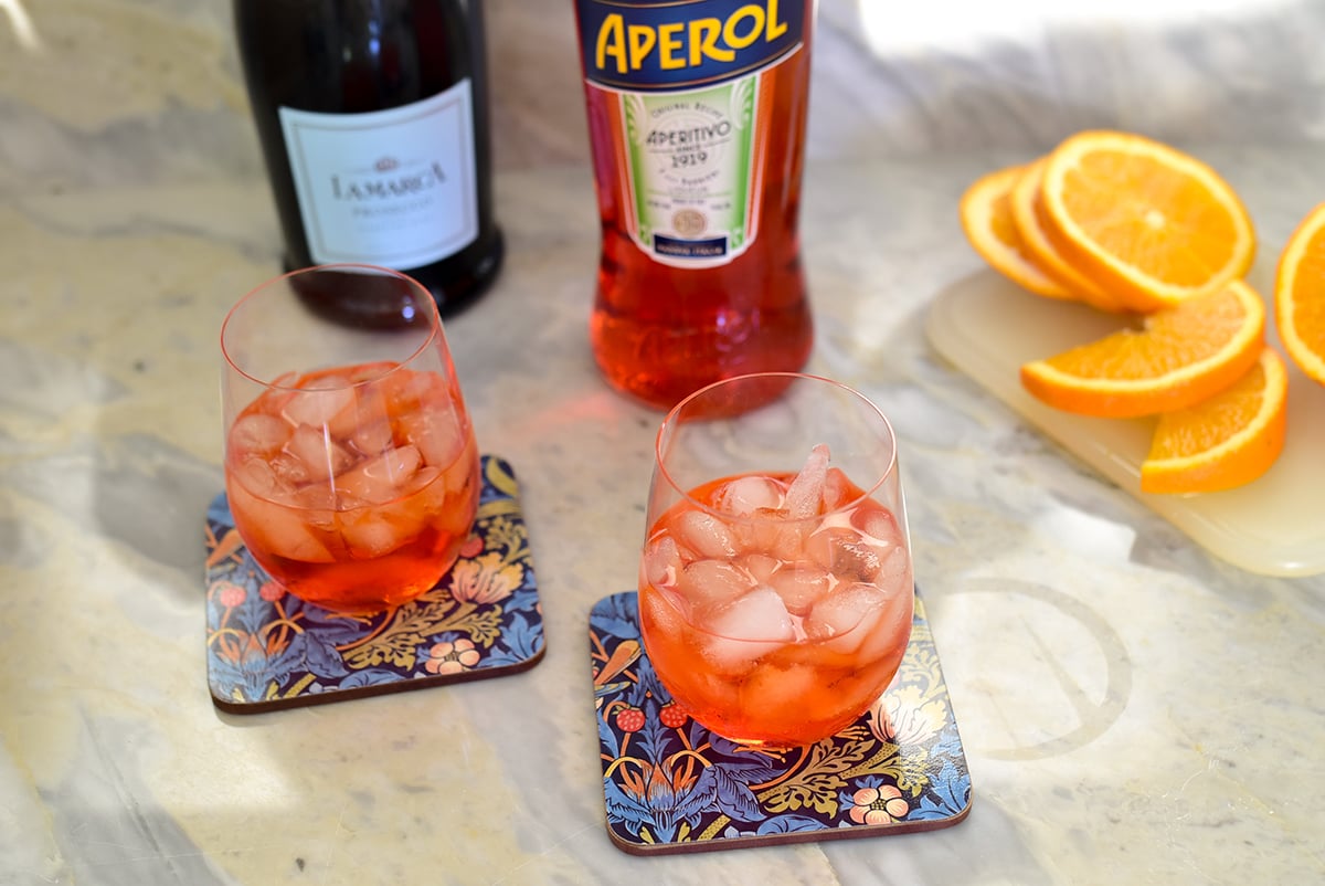 wine glasses with ice and orange liquid with aperol in the background