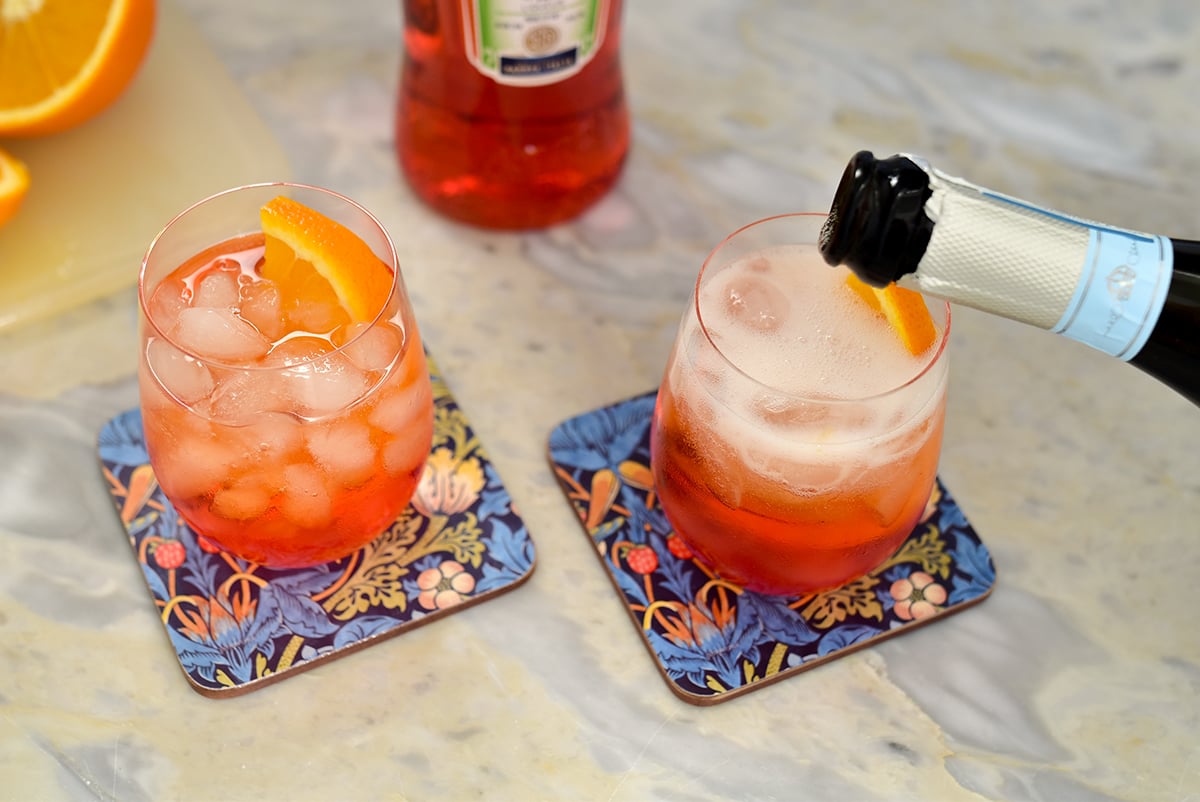 prosecco poured into a wine glass with ice and an orange liquid 