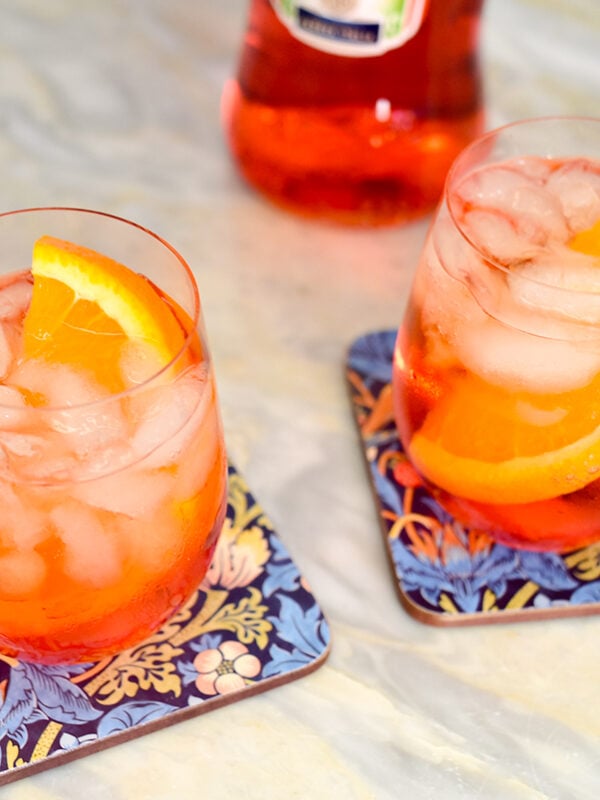 two aperol spritz cocktails in wine glasses with orange wedges in them