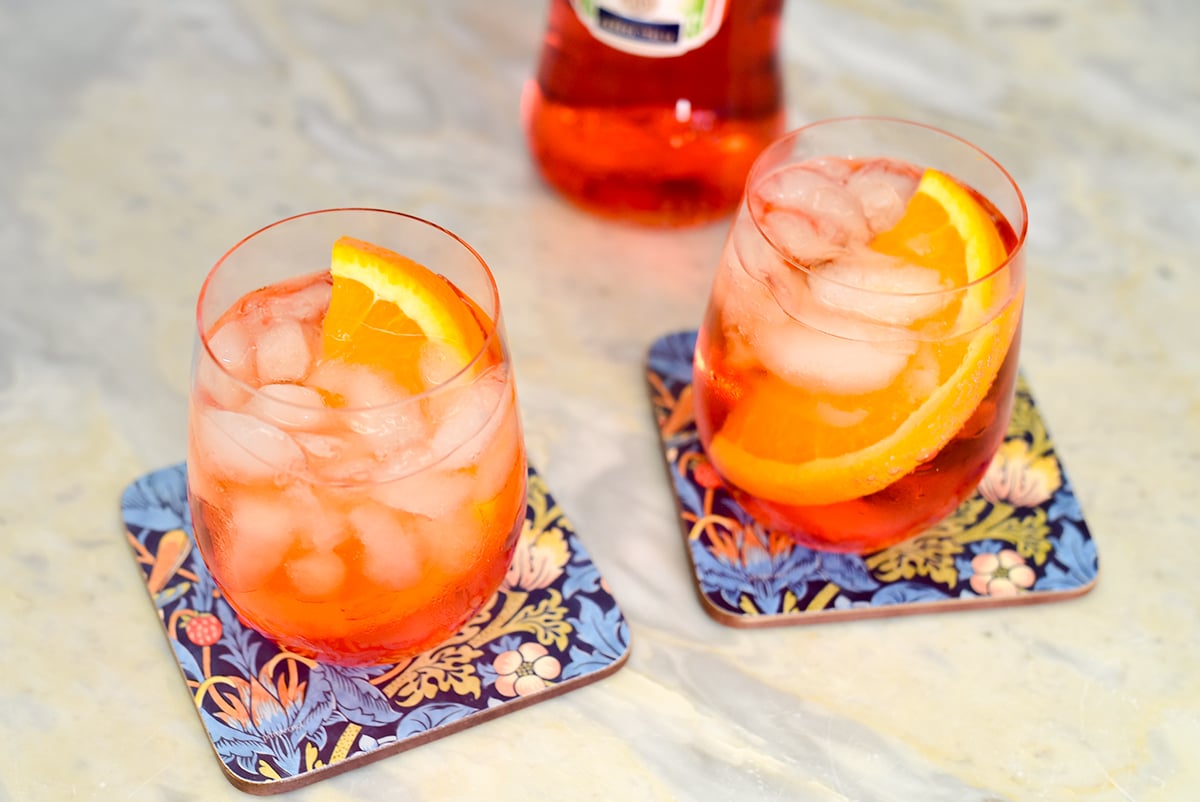 two aperol spritz cocktails in wine glasses with orange wedges in them