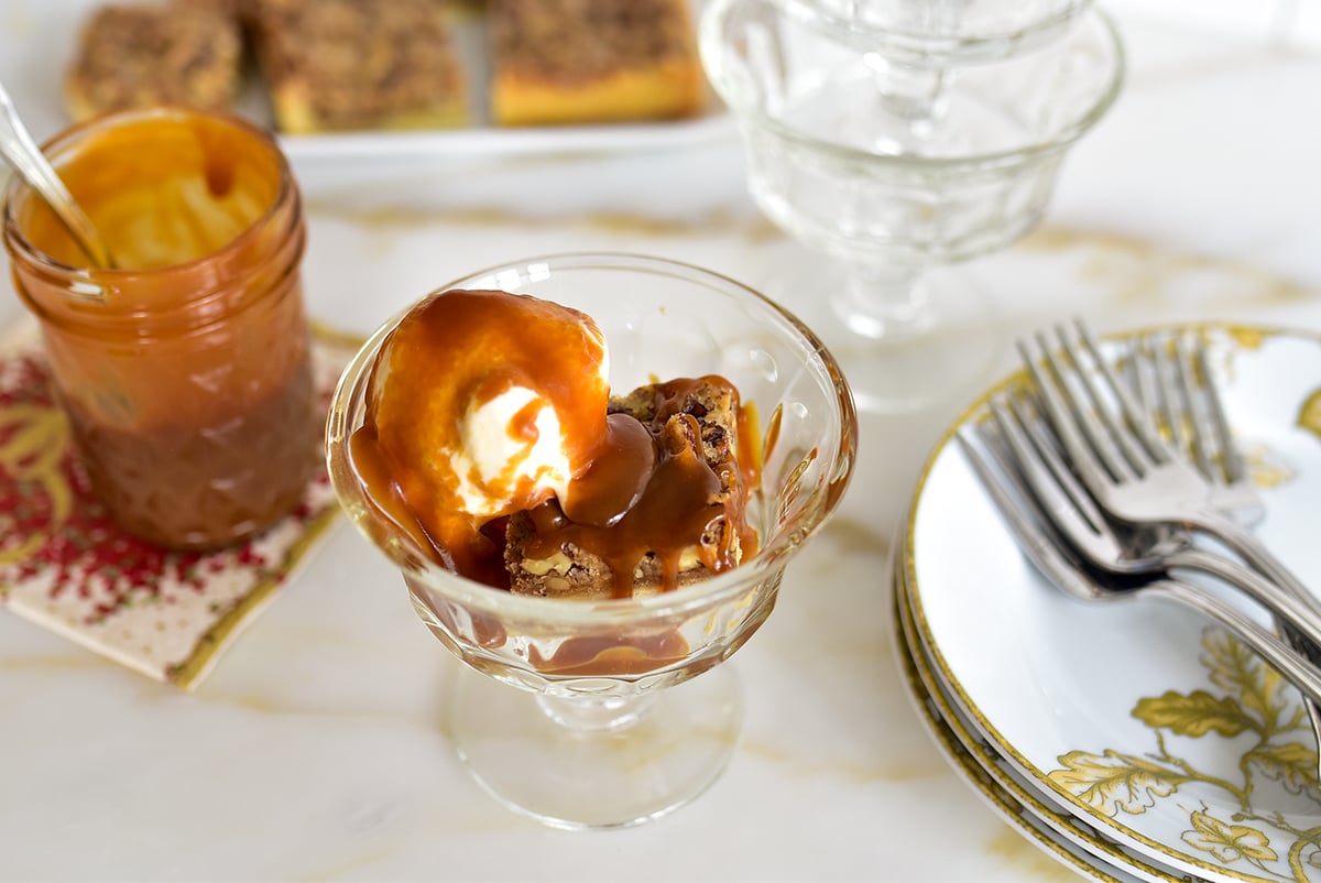 pecan pie bar in a footed glass dish with vanilla ice cream scoop and caramel sauce on top