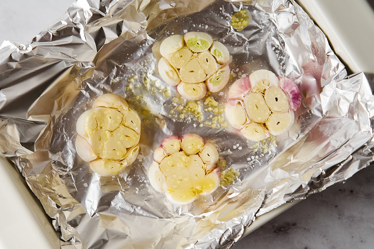 heads of garlic with the tops trimmed off on a sheet of aluminum foil