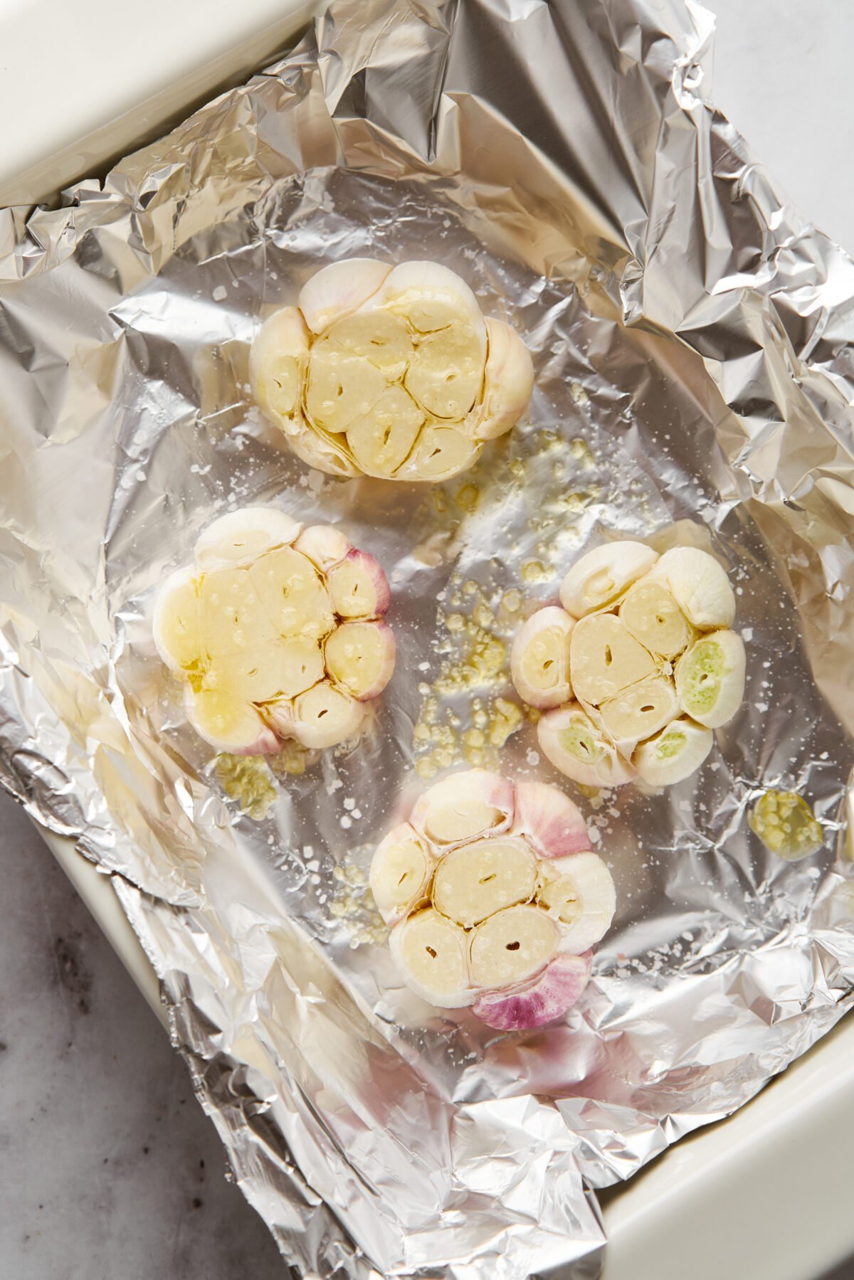 Garlic heads with the tops cut off, on a sheet of aluminum foil