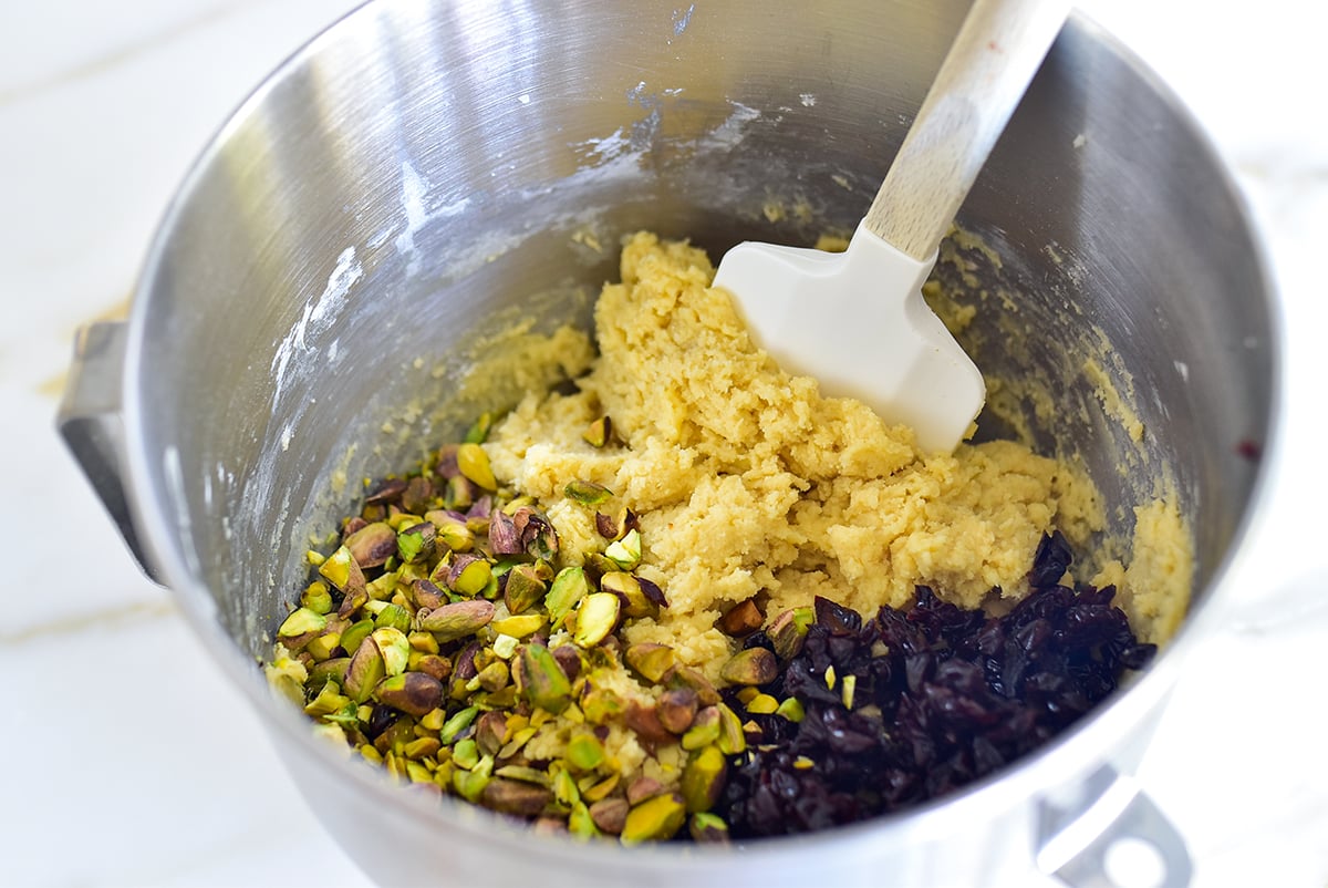 Dough for biscotti in a mixing bowl with pistachios and dried cherries