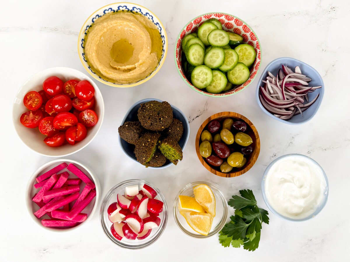 Ingredients for falafel bowls in small bowls on a white countertop