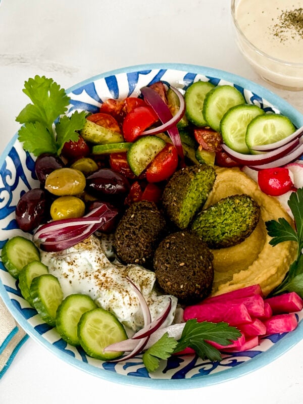 Falafel bowl in a blue and white bowl with a fork beside it along with tahini sauce and lemon slices in small bowls