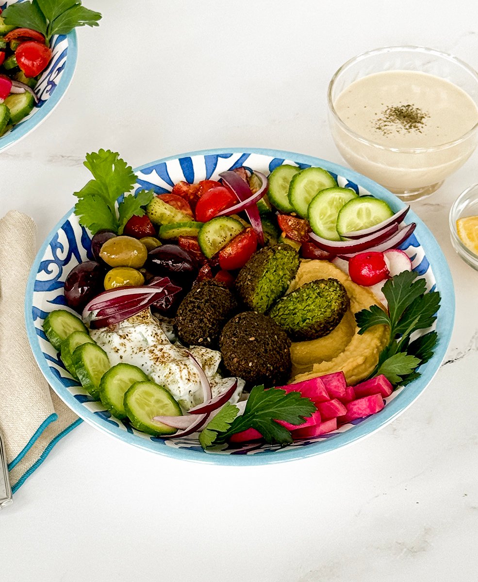 Falafel bowl with vegetables in a blue and white bowl with a bowl of tahini sauce on the side