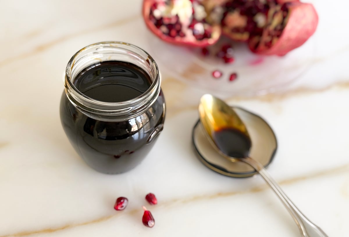 pomegranate molasses in a jar with pomegranate seeds and a spoon