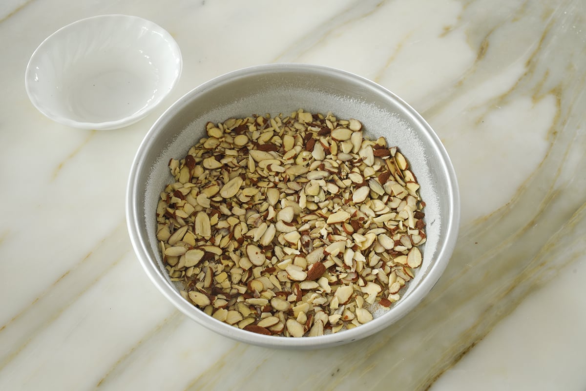 A round cake pan with sliced almonds in the base of it