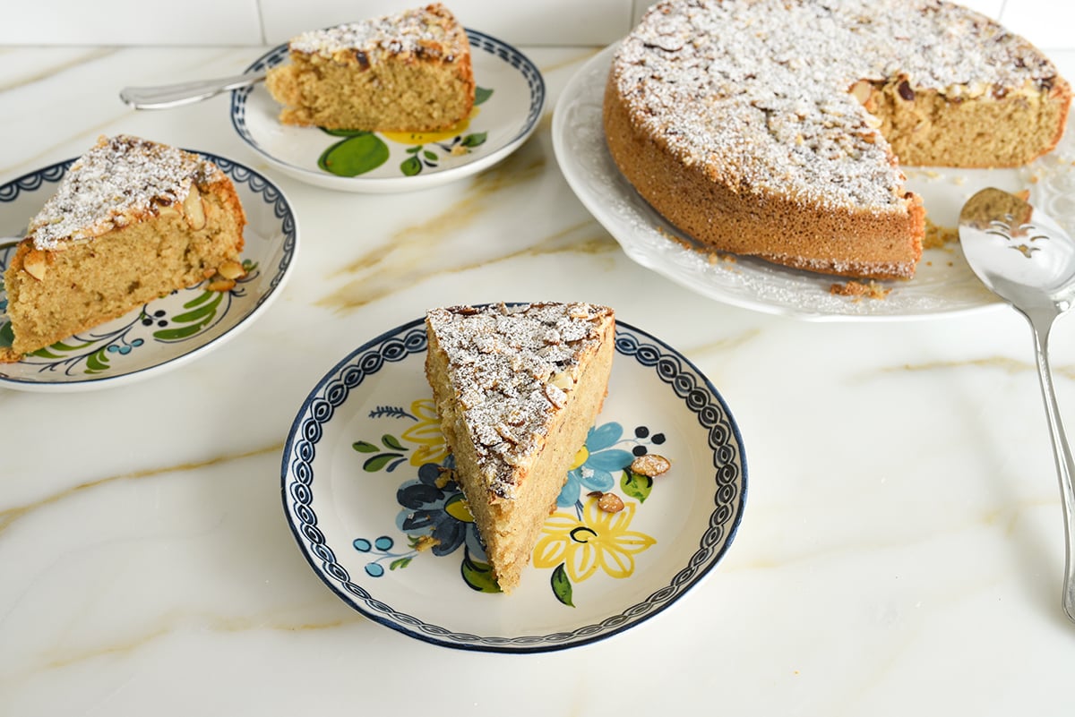 Cardamom cake slice on a flowered plate with the cut cake in the background on a marble countertop