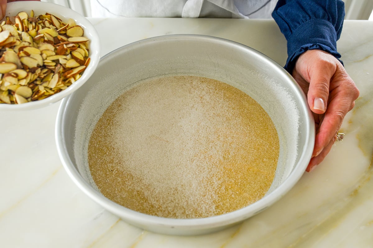 Round cake pan with sugar in it and almonds in a bowl off to the side