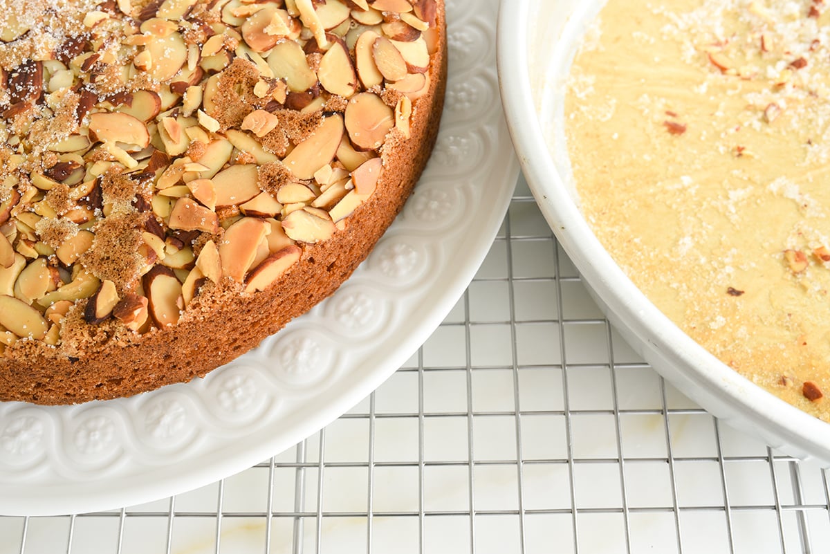 An almond topped cake on a white plate with the empty cake pan next to it