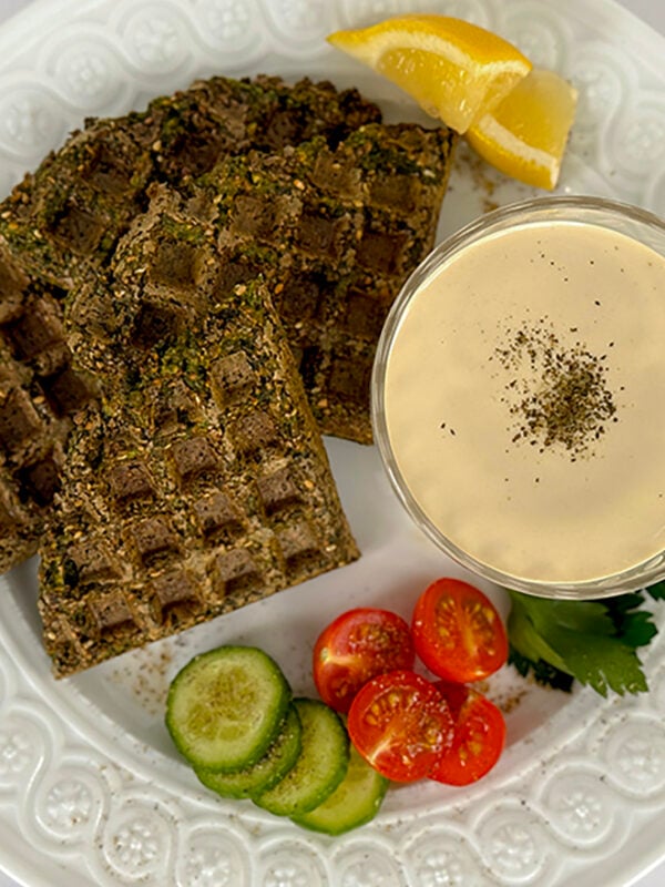 Falafel waffle on a white plate with tahini sauce