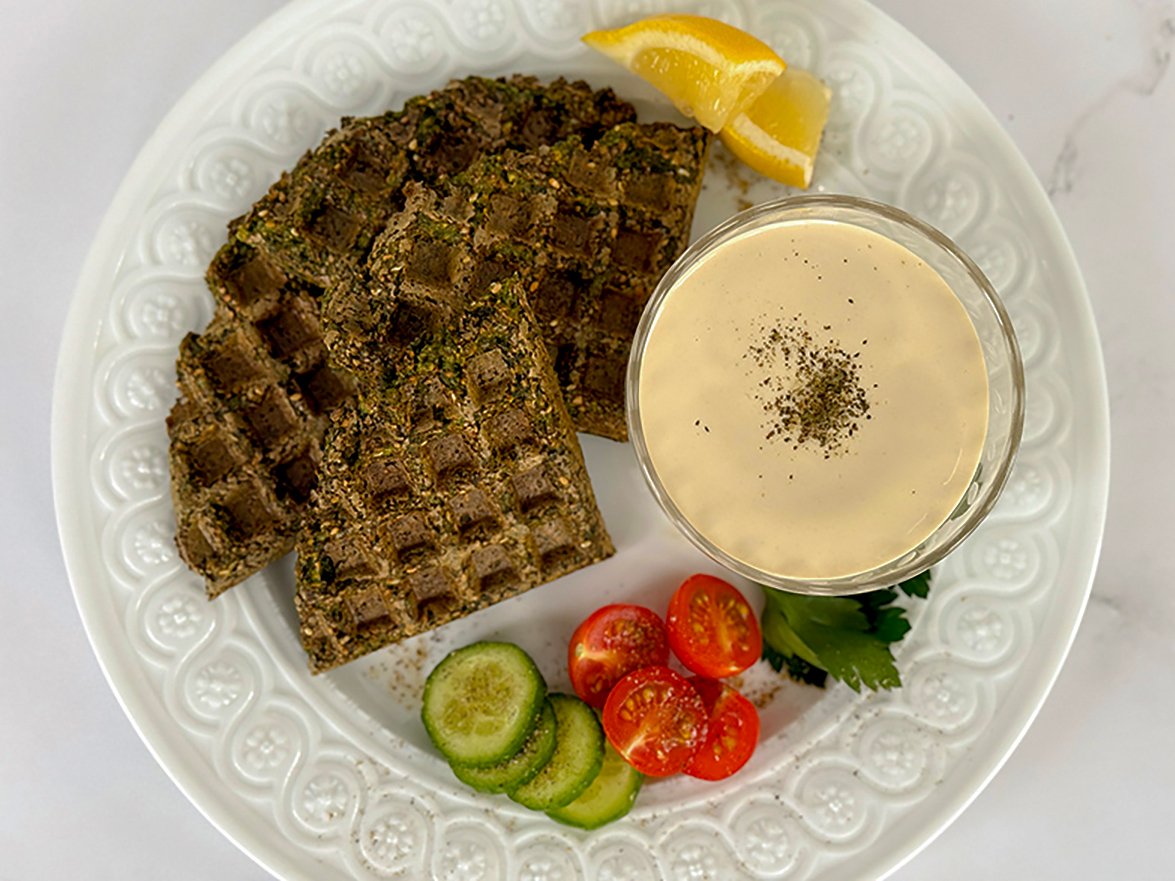 Falafel waffle on a white plate with tahini sauce