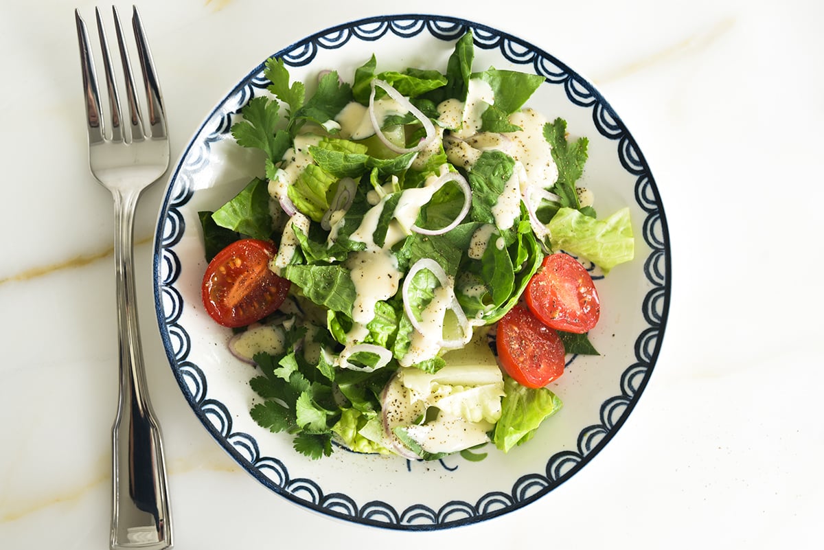 A mixed green salad on a salad plate with a blue rim and a fork next to it