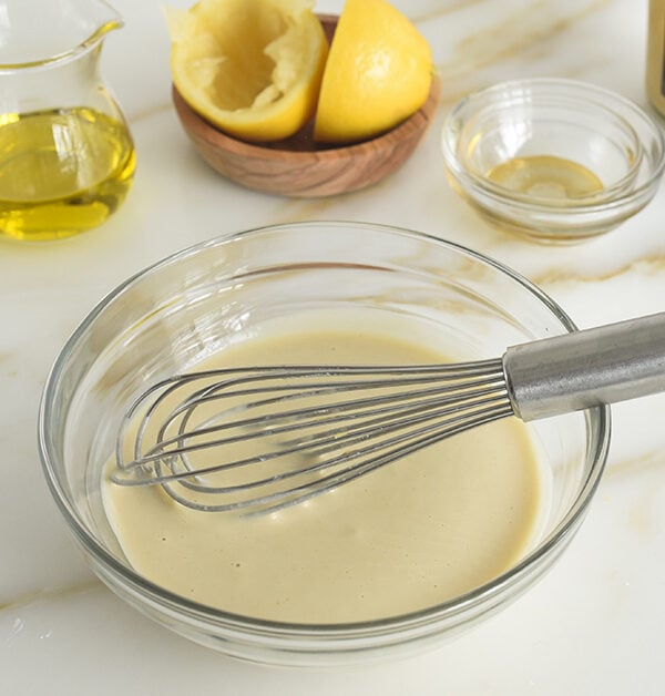 Tahini dressing in a glass bowl with a whisk