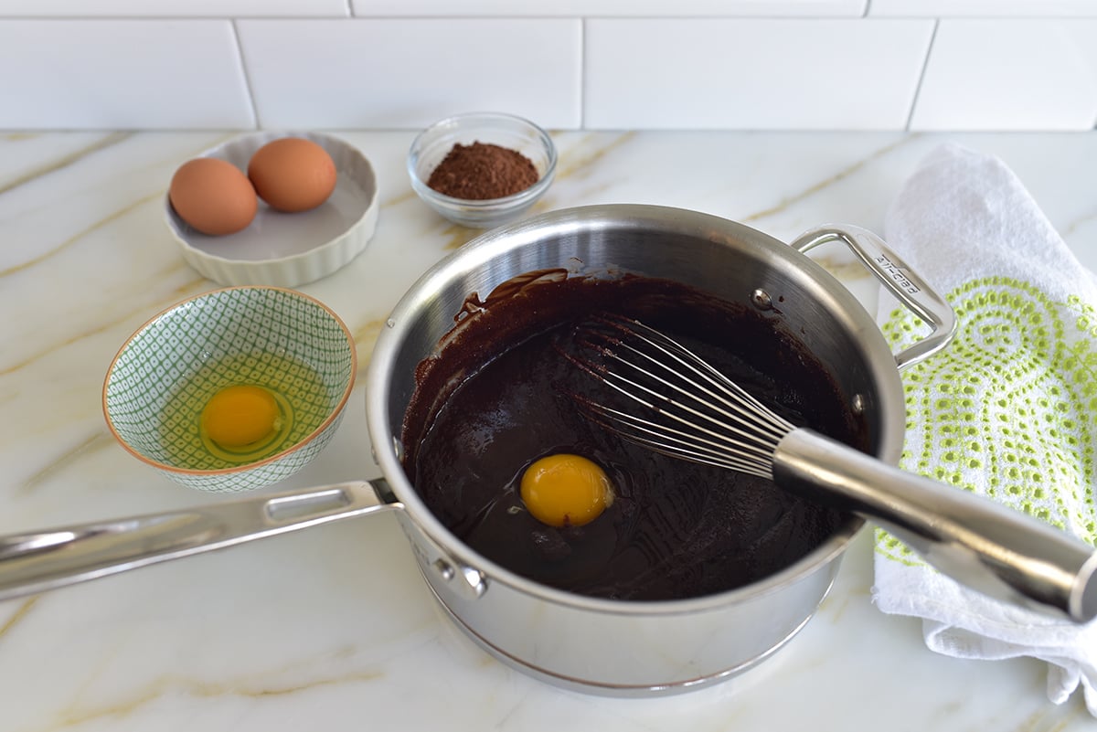 batter for flourless chocolate cake in a pot with a whisk and an egg in it