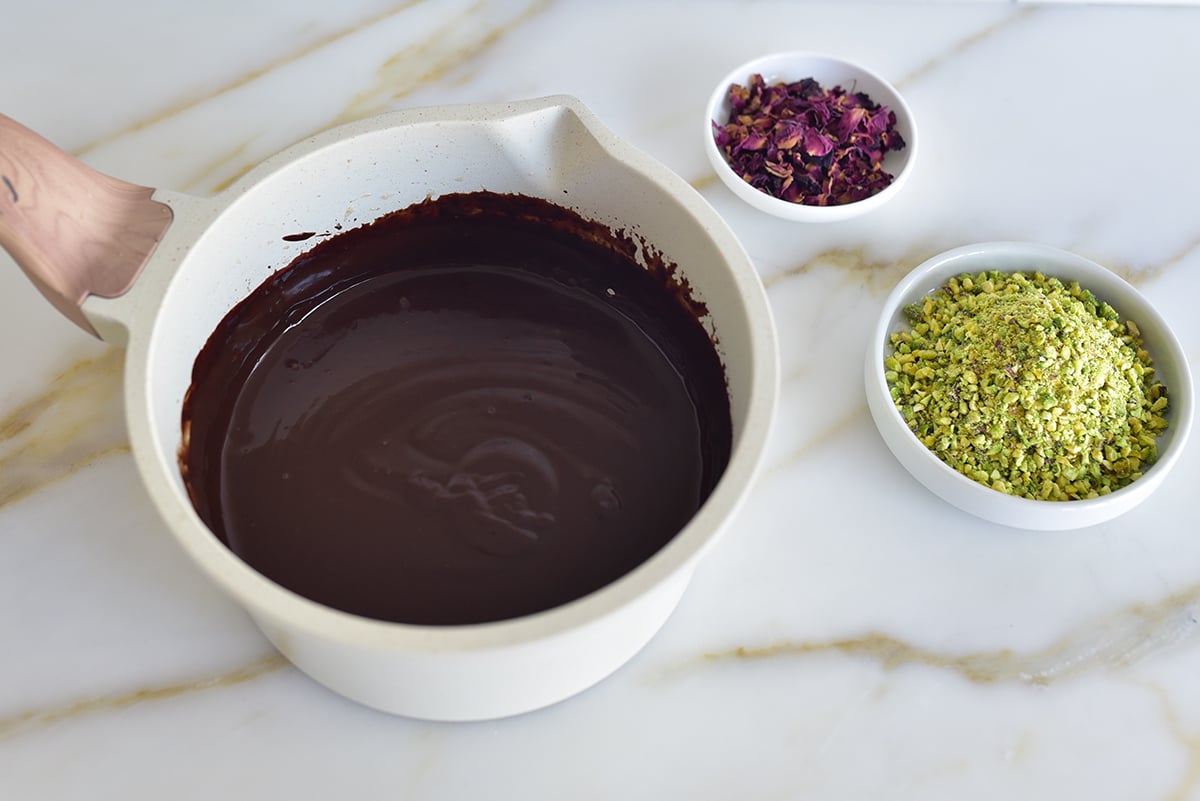 chocolate glaze in a white pot with pistachos in a bowl beside it