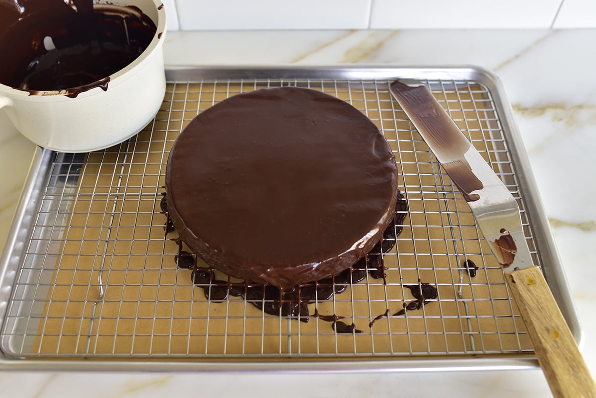 a glazed round cake on a wire rack with an offset spatula next to it