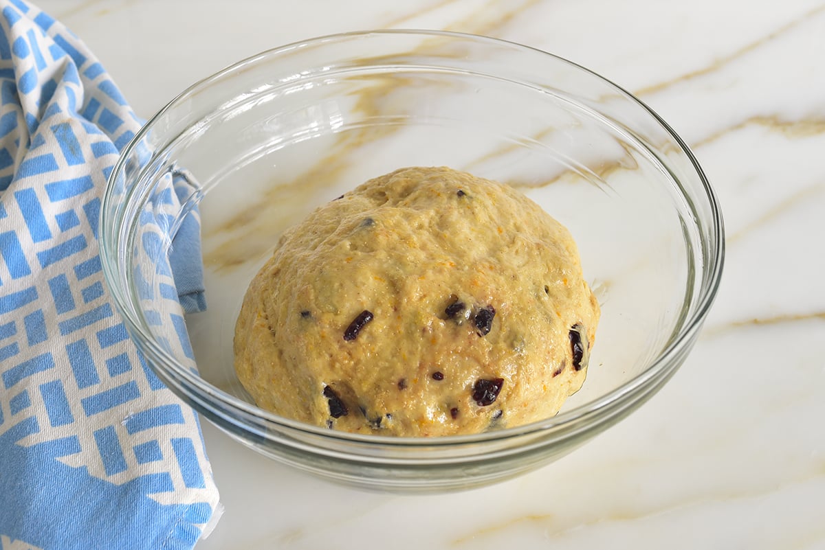 dough with dried fruit in it in a glass bowl with a blue towel beside it